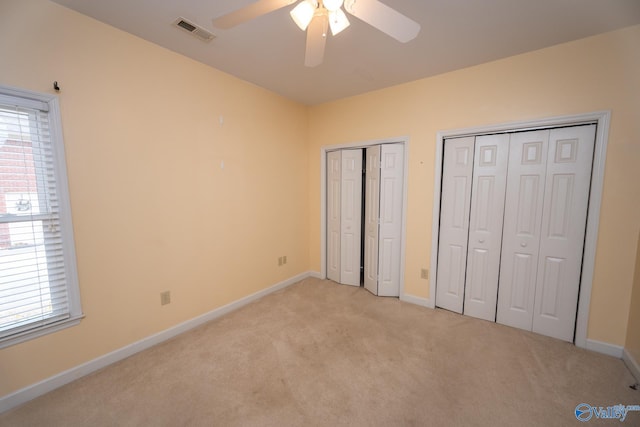 unfurnished bedroom featuring light colored carpet, visible vents, two closets, and baseboards