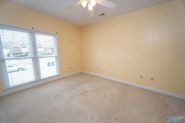 empty room featuring a ceiling fan, light colored carpet, visible vents, and baseboards