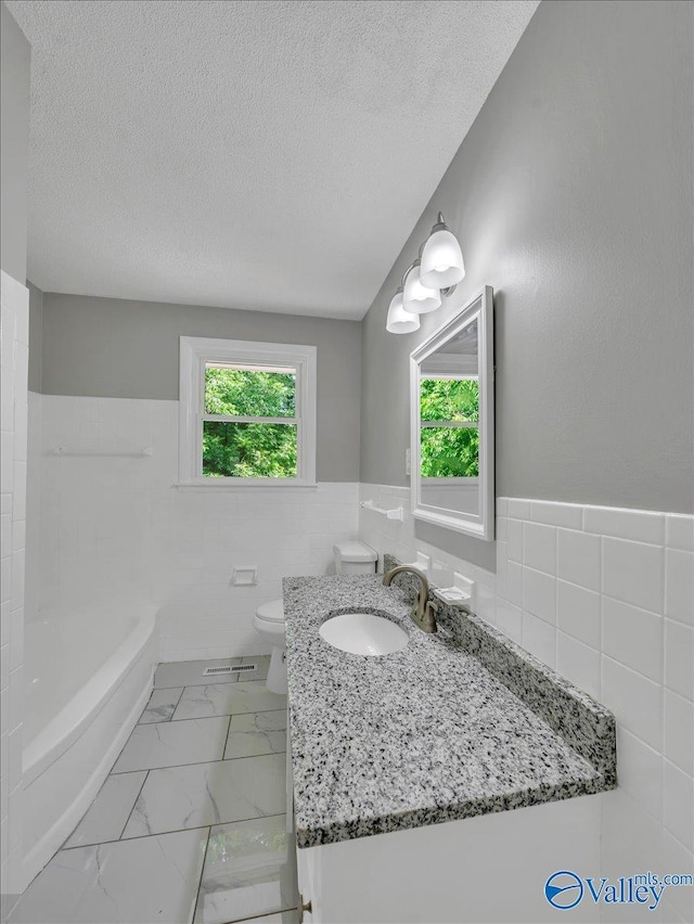 2612 Valley Brook Dr, Huntsville, AL 35811 - bathroom with tile walls, a tub, vanity, wainscoting, and a textured ceiling