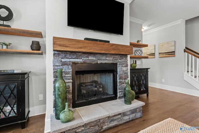 living room with a stone fireplace, dark wood-type flooring, baseboards, ornamental molding, and stairway