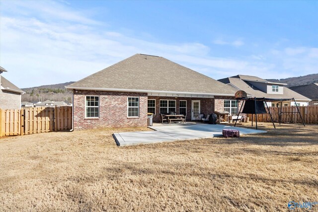 rear view of property featuring a patio area, brick siding, a fenced backyard, and roof with shingles