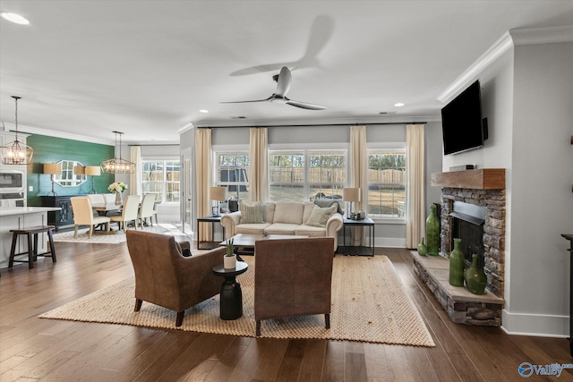 living room with baseboards, dark wood finished floors, ceiling fan, crown molding, and a fireplace