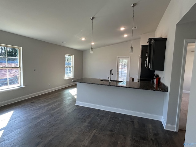 kitchen with a sink, a healthy amount of sunlight, dark wood-style floors, and dark stone countertops