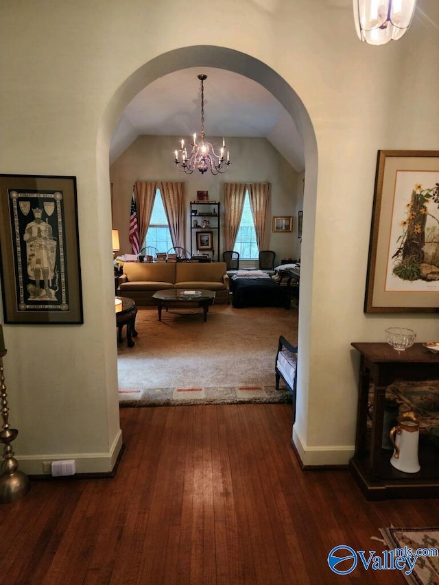 corridor featuring arched walkways, dark wood-style flooring, lofted ceiling, a chandelier, and baseboards