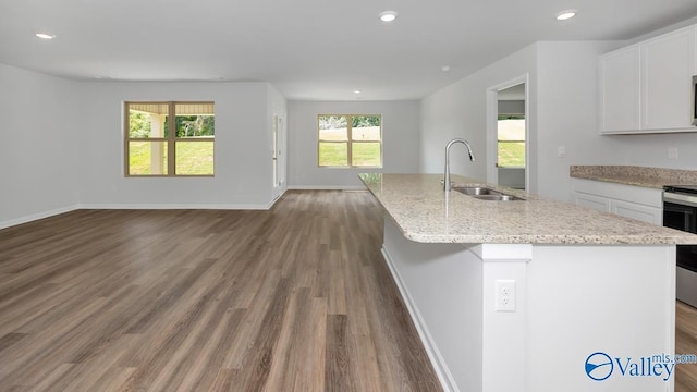 kitchen with a kitchen island with sink, a sink, white cabinets, open floor plan, and light stone countertops