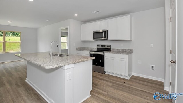 kitchen featuring a center island with sink, appliances with stainless steel finishes, a sink, and wood finished floors