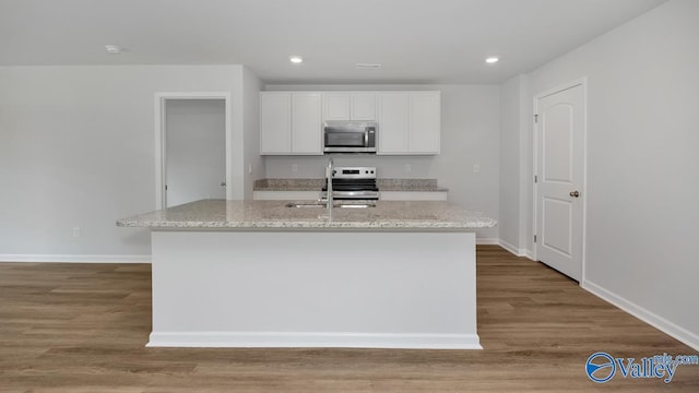 kitchen featuring appliances with stainless steel finishes, wood finished floors, white cabinetry, and light stone countertops