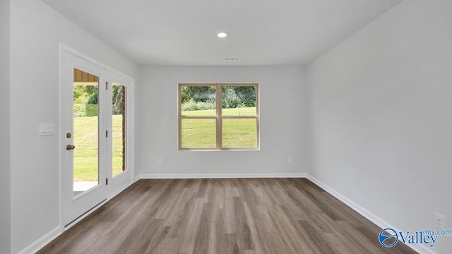 unfurnished room featuring wood finished floors, a wealth of natural light, and baseboards