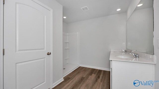 bathroom featuring visible vents, a sink, wood finished floors, baseboards, and walk in shower