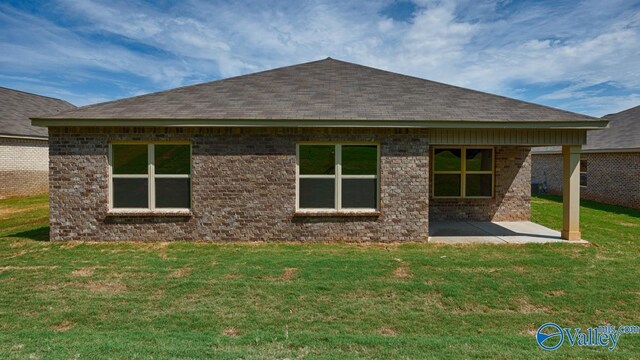 rear view of house with a yard, brick siding, a patio, and roof with shingles