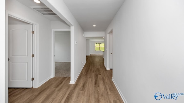 hall featuring visible vents, baseboards, and wood finished floors