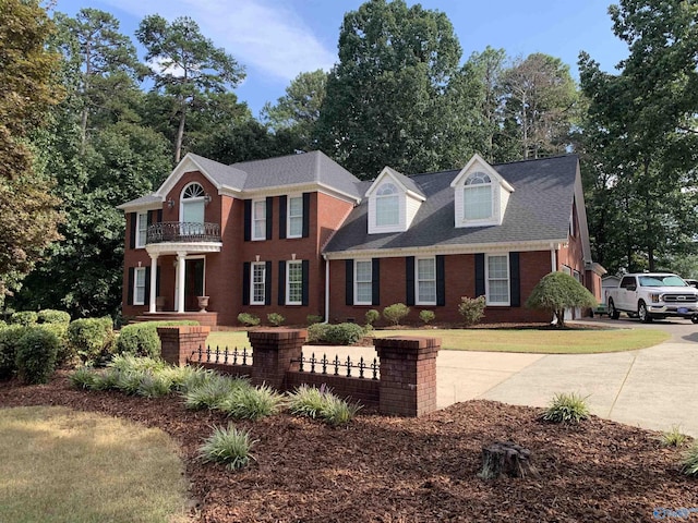 view of front of house with a fenced front yard, brick siding, a shingled roof, a balcony, and a front lawn