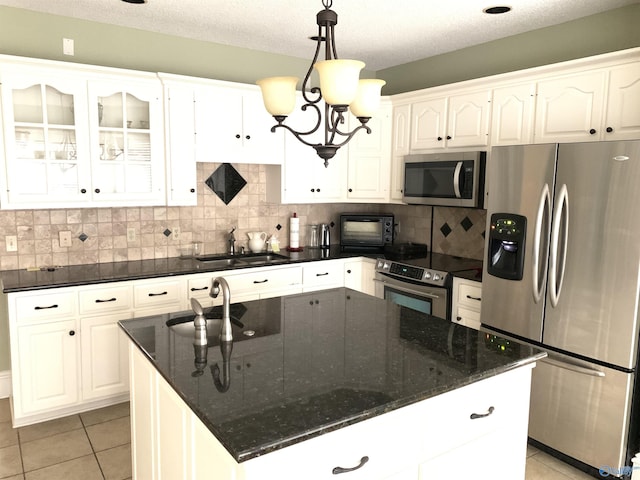 kitchen with light tile patterned floors, stainless steel appliances, a sink, white cabinetry, and tasteful backsplash