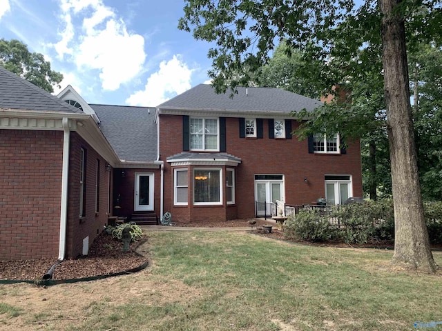 view of front of property featuring a shingled roof, a front yard, and brick siding