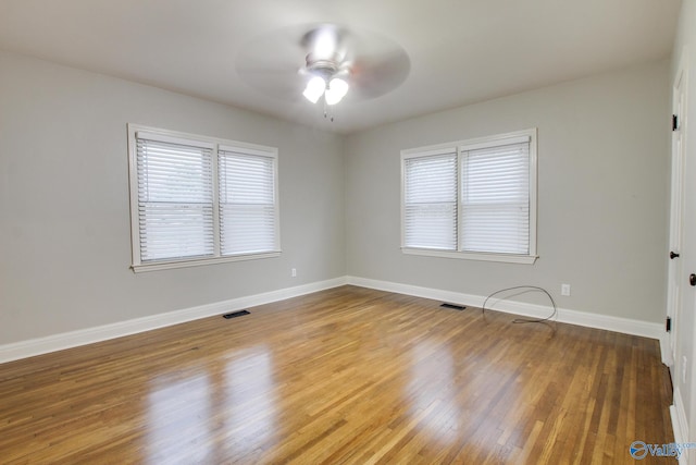 spare room featuring baseboards, visible vents, a ceiling fan, and wood finished floors