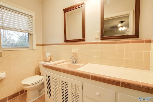 half bath with a wainscoted wall, tile patterned floors, toilet, vanity, and tile walls