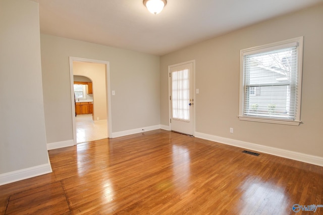 spare room featuring baseboards, visible vents, arched walkways, and light wood-type flooring