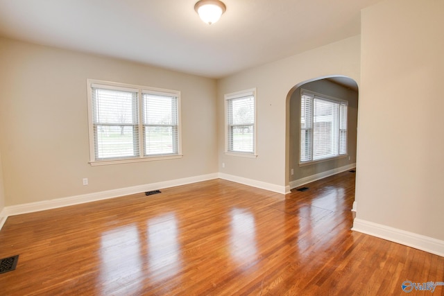 unfurnished room featuring visible vents, arched walkways, baseboards, and wood finished floors