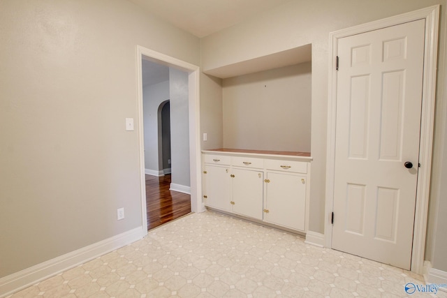 interior space with baseboards, arched walkways, and light floors