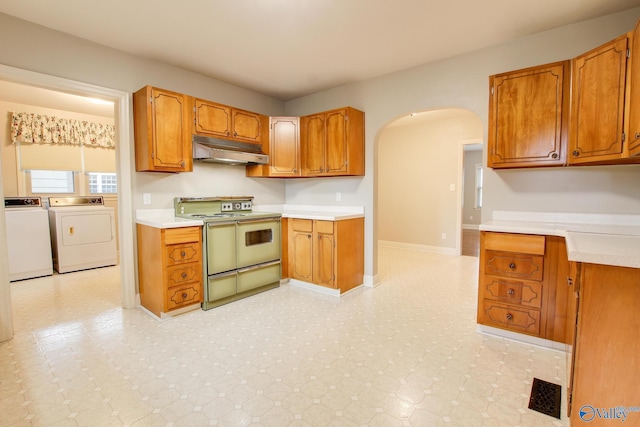 kitchen featuring light floors, arched walkways, under cabinet range hood, washer and dryer, and range with two ovens