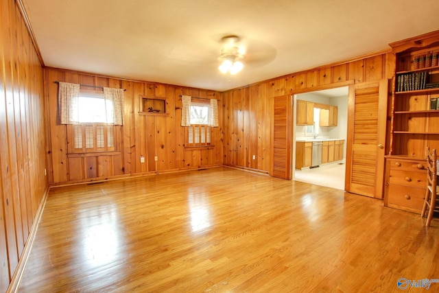 unfurnished living room with plenty of natural light, wooden walls, light wood finished floors, and ceiling fan