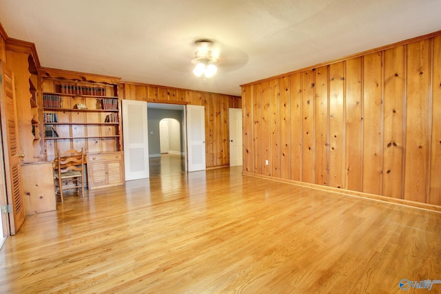 empty room with arched walkways, wood finished floors, wooden walls, and a ceiling fan