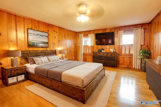 bedroom with light wood-style floors, wood walls, and multiple windows