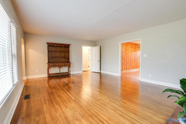 unfurnished living room with arched walkways, baseboards, visible vents, and light wood-style floors