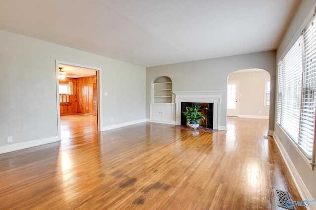 unfurnished living room featuring baseboards, visible vents, built in shelves, and light wood finished floors
