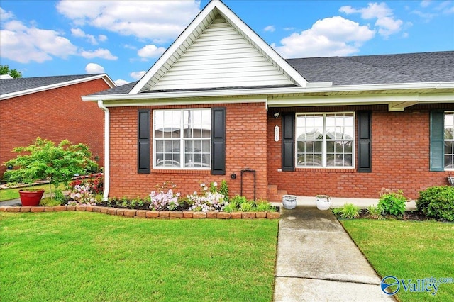 view of front of home with a front lawn, brick siding, and roof with shingles