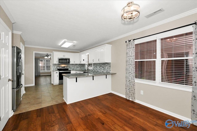 kitchen featuring stainless steel appliances, visible vents, ornamental molding, a sink, and a peninsula