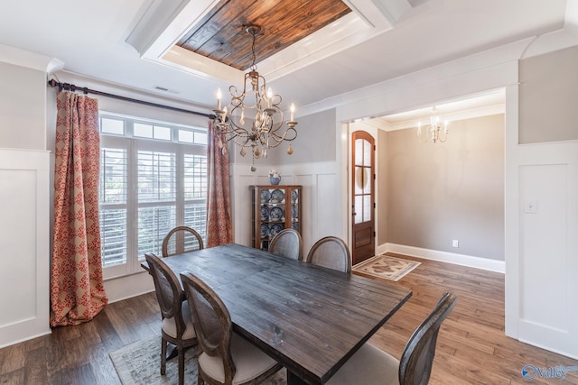 dining area with ornamental molding, wood finished floors, a tray ceiling, a chandelier, and a decorative wall