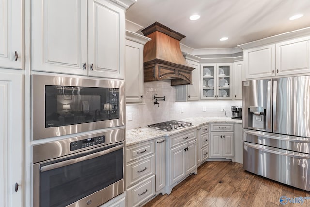 kitchen featuring dark hardwood / wood-style flooring, tasteful backsplash, custom exhaust hood, light stone counters, and stainless steel appliances