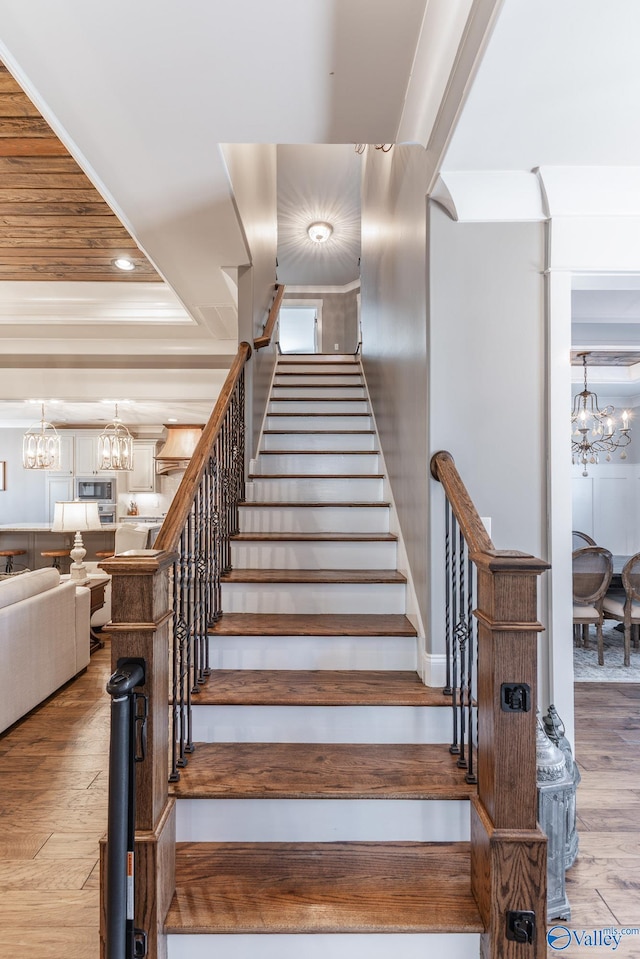 staircase with a raised ceiling, a chandelier, and wood-type flooring