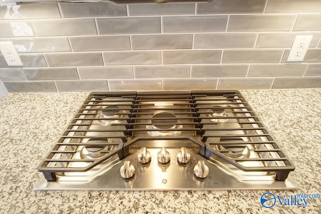 room details with backsplash, light stone counters, and stainless steel gas cooktop