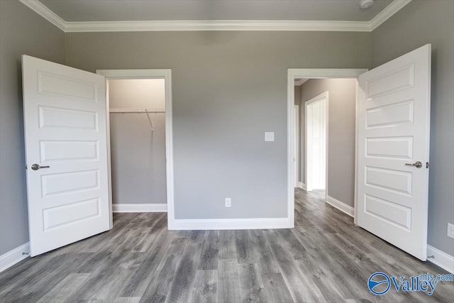 unfurnished bedroom featuring hardwood / wood-style flooring, a closet, a walk in closet, and ornamental molding