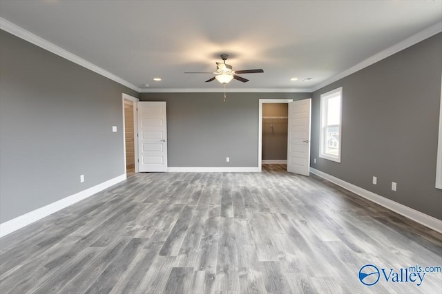 unfurnished bedroom featuring a walk in closet, ceiling fan, crown molding, and a closet