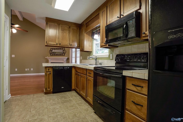 kitchen with a sink, black appliances, brown cabinetry, tile counters, and light tile patterned floors