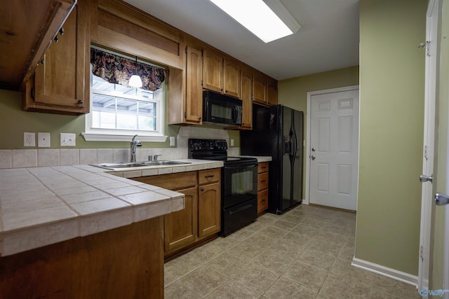 kitchen with tile countertops, light tile patterned floors, a sink, black appliances, and brown cabinetry