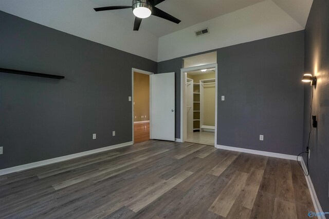 unfurnished bedroom with lofted ceiling, wood finished floors, visible vents, a walk in closet, and baseboards