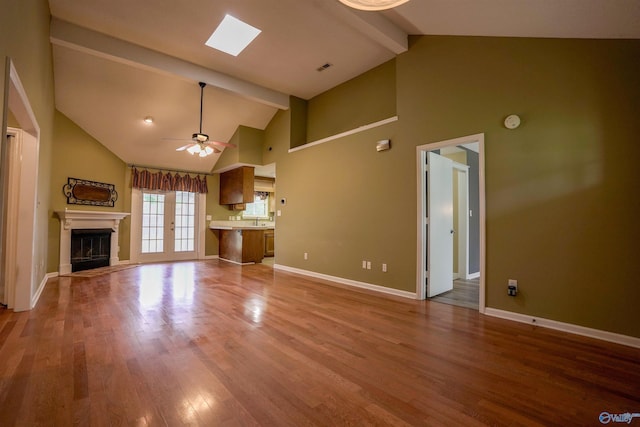 unfurnished living room with beam ceiling, a glass covered fireplace, a ceiling fan, wood finished floors, and high vaulted ceiling