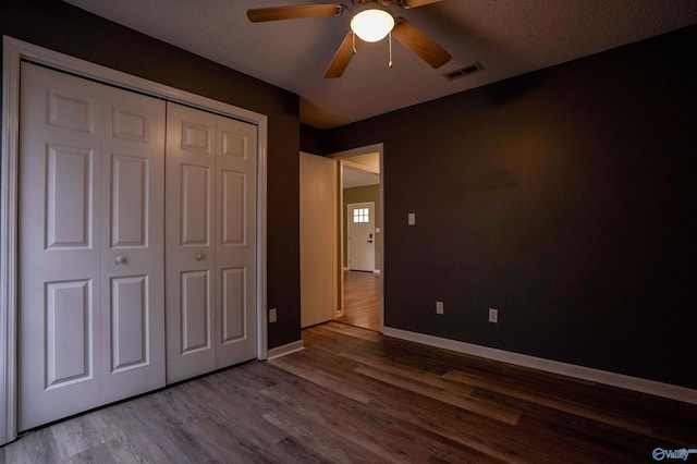 unfurnished bedroom featuring wood finished floors, visible vents, a closet, baseboards, and ceiling fan