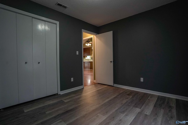 unfurnished bedroom with a closet, wood finished floors, visible vents, and baseboards