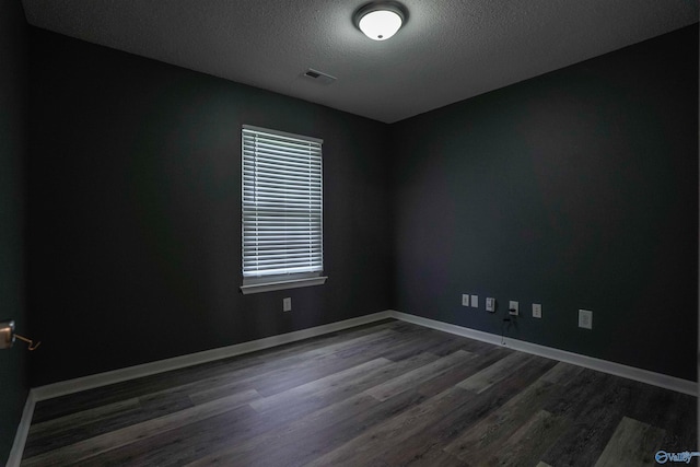 empty room featuring dark wood-type flooring, a textured ceiling, visible vents, and baseboards