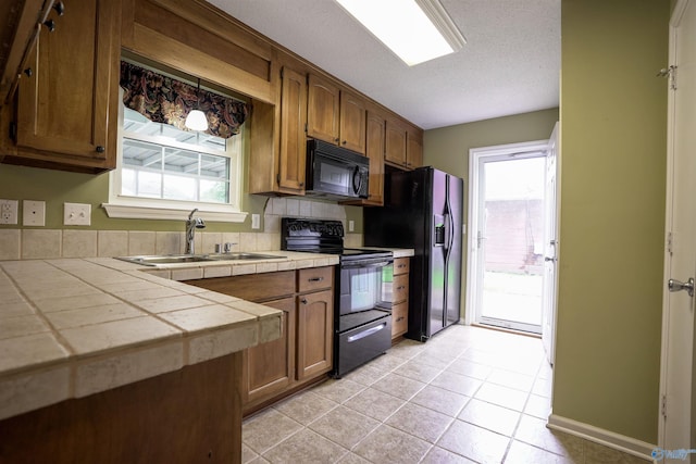 kitchen with tile counters, light tile patterned floors, a sink, black appliances, and a textured ceiling