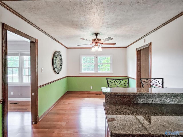 unfurnished room with a textured ceiling, wood finished floors, a ceiling fan, baseboards, and crown molding