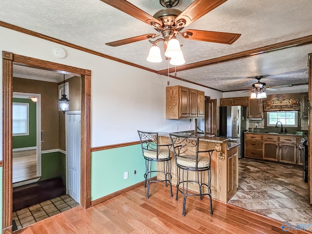 kitchen featuring brown cabinetry, ornamental molding, a breakfast bar area, freestanding refrigerator, and light wood-type flooring