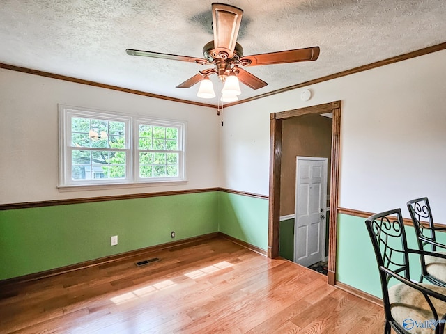 spare room featuring a textured ceiling, ceiling fan, wood finished floors, visible vents, and ornamental molding