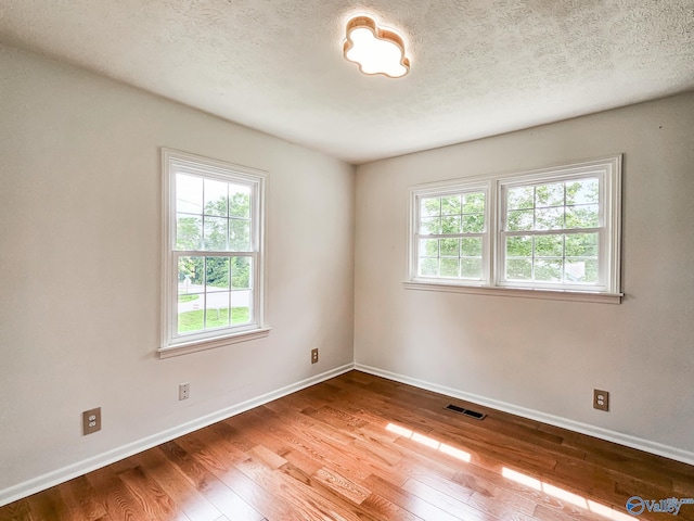 spare room with a textured ceiling, wood finished floors, visible vents, and baseboards