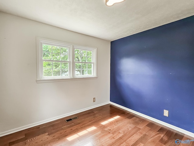 empty room featuring visible vents, a textured ceiling, baseboards, and wood finished floors